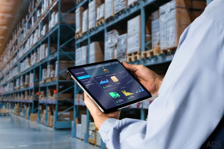 Personne qui tient une tablette dans l'allée d'un entrepôt, il est en train de faire la gestion d'inventaire de son entreprise